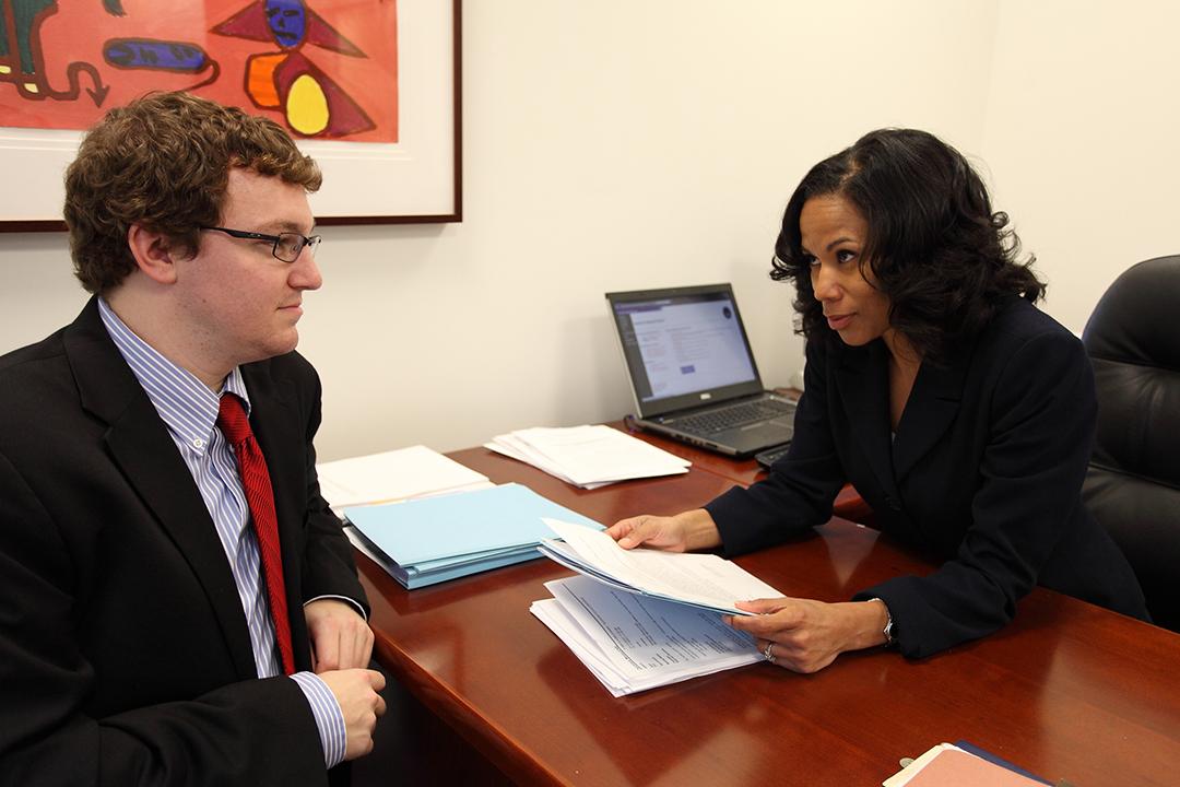 A male student and female faculty member sitting at a desk talking and looking at a paper.